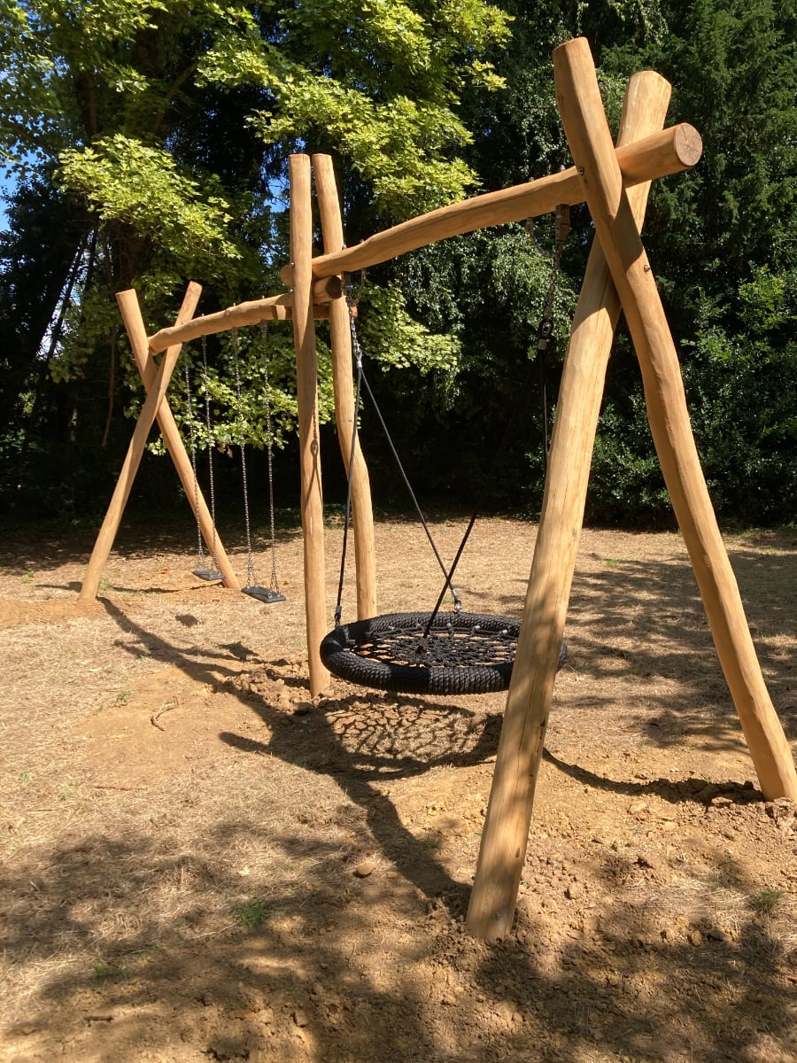 Een houten schommelconstructie in de tuin van de Pastorie, met twee traditionele schommels en een mand-schommel.
